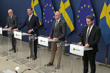 De fyra medverkande fotograferade i helfigur snett framifrån vid vart sin talarstol.