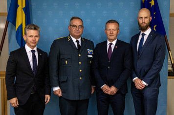 Försvarsminister Pål Jonson, överbefälhavare Michael Claesson från Försvarsmakten, Mikael Frisell, generaldirektör för MSB, och minister för civilt försvar Carl-Oskar Bohlin stående framför en blå vägg med flaggor.