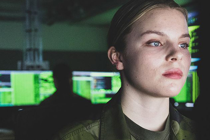 Soldat i uniform sitter i ett rum med flera datorskärmar.