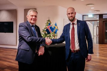 Minister för civilt försvar Carl-Oskar Bohlin och Islands justitieminister Jón Gunnarsson skakar hand framför ett bord med en isländsk och en svensk flagga på. Bakom bordet står en julgran.