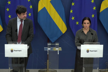 Kulturminister Parisa Liljestrand och ytterligare en person står vid var sin talarstol. Det är flaggor i fonden.