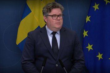 Justitieminister Gunnar Strömmer i talarstol framför fond av svenska flaggor