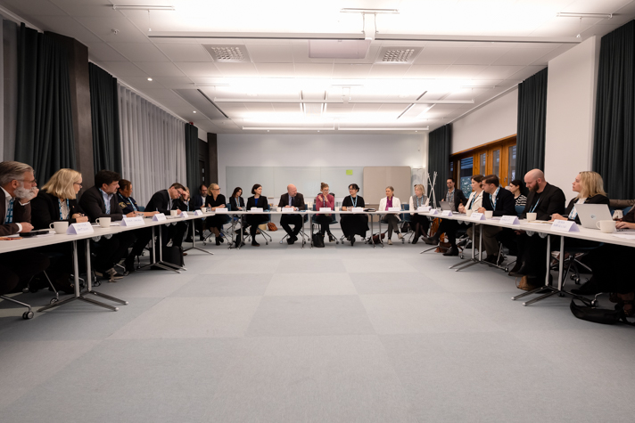 Bild på hela arbetsgruppen som sitter i en hästsko i mötesrum.