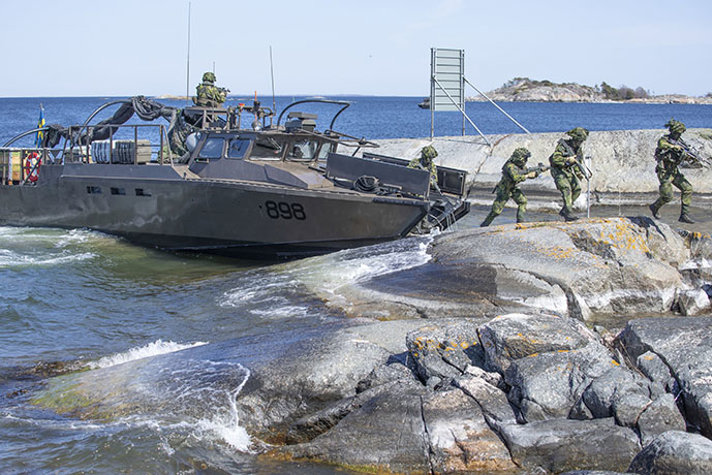 Amfibiesoldater hoppar ur en stridsbåt 90 och avancerar upp längs kala klippor