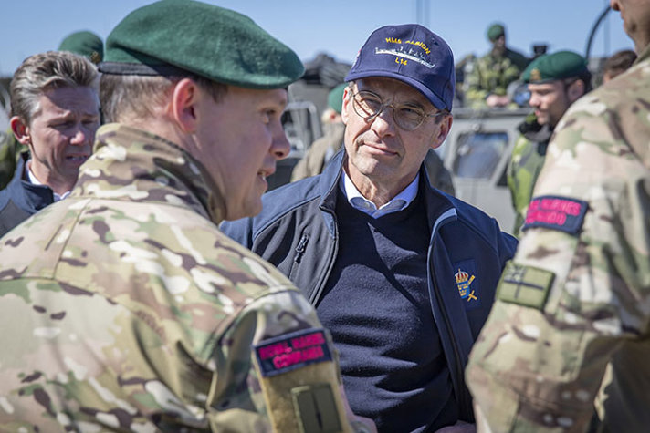 Ulf Kristersson iklädd en marinblå keps med texten HMS Albion står och pratar med befäl ur Royal Marines