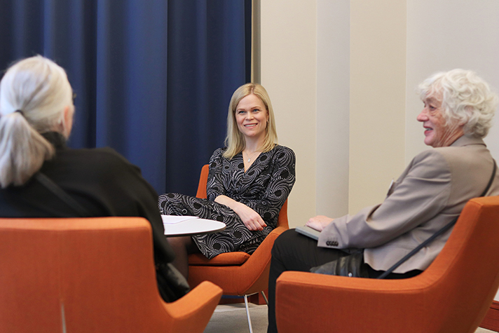 Paulina Brandberg sitter i en fåtölj och ler. Mitt emot henne syns ryggtavlorna på två personer som hon samtalar med.