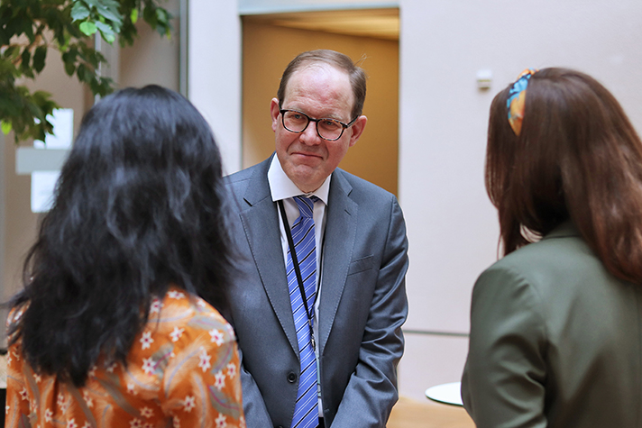 Två personer står med ryggen mot kameran. De samtalar med statssekreterare Martin Andreasson som står mitt emot dem och lyssnar.