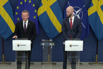 De två medverkande står vid var sin talarpulpet. Det är fanor i fonden.