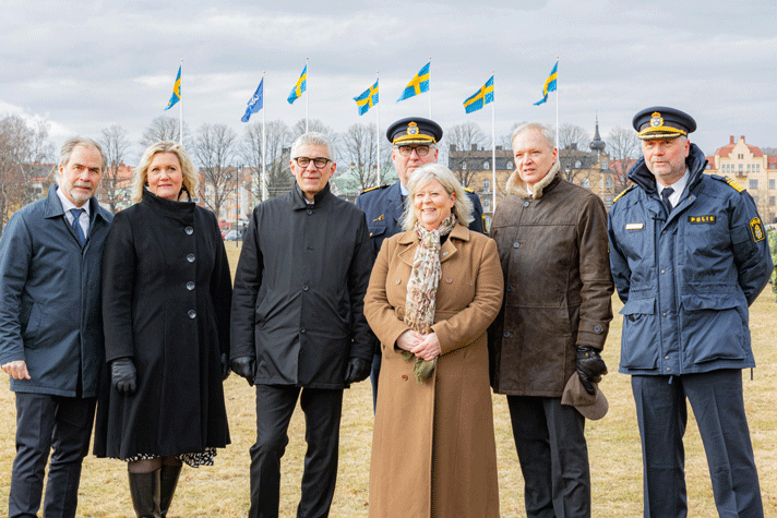 Camilla stående utomhus omgiven av militärer i uniform.