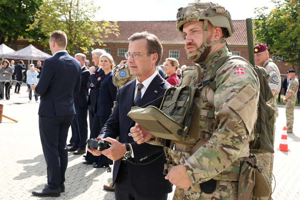 Statsminister Ulf Kristersson står bredvid en soldat. Statsministern håller i en konsol.