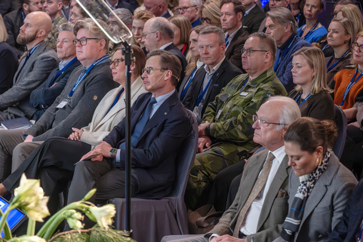 Bild snett ovanifrån på publiken med statsråd och kungligheter på första raden.