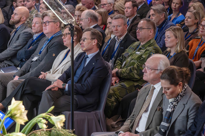 Bild snett ovanifrån på publiken med statsråd och kungligheter på första raden.