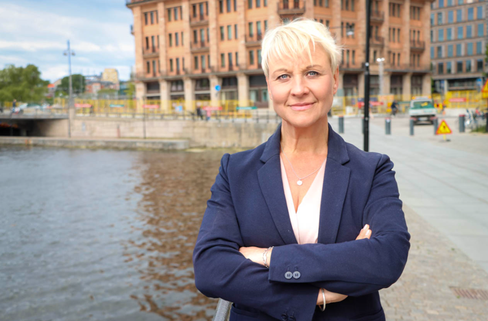 Anna Tenje står vid vattnet i stadsmiljö vänd mot kameran i mörkblå kavaj.