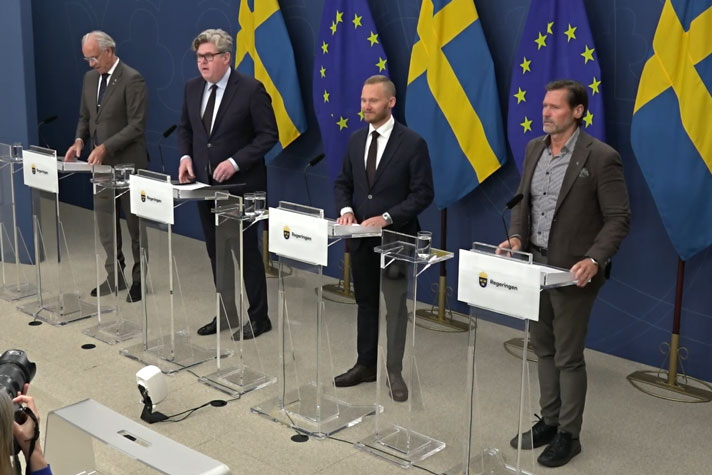 Fyra personer avbildade snett uppifrån står vid var sin talarpulpet.