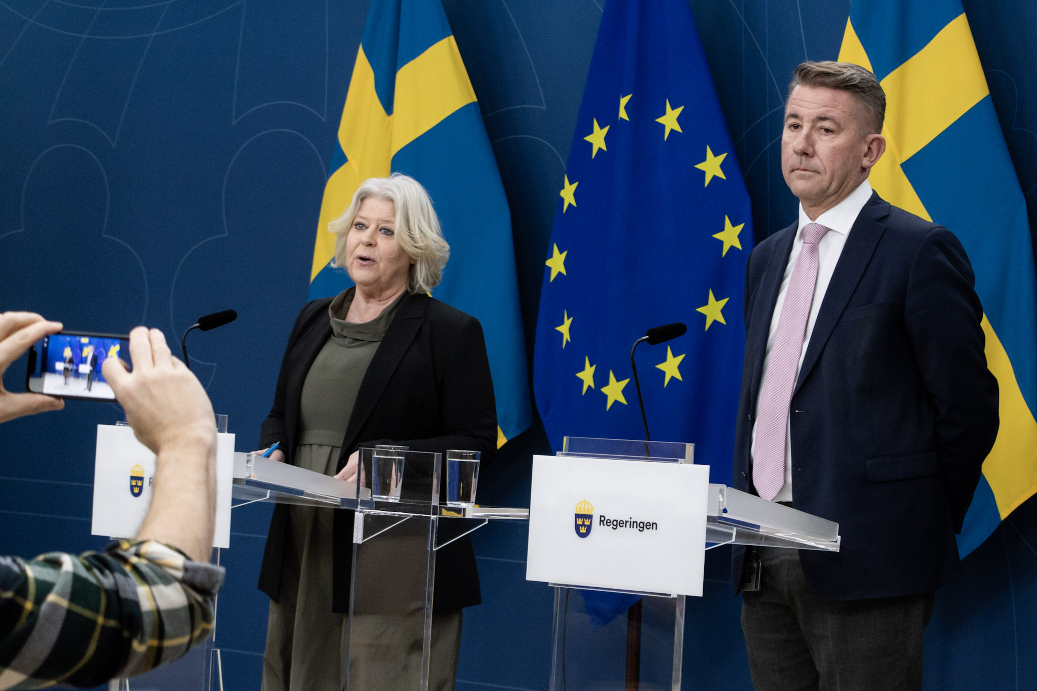 Camilla Waltersson Grönvall och Martin Valfridsson står bakom var sitt podium i regeringens pressrum.