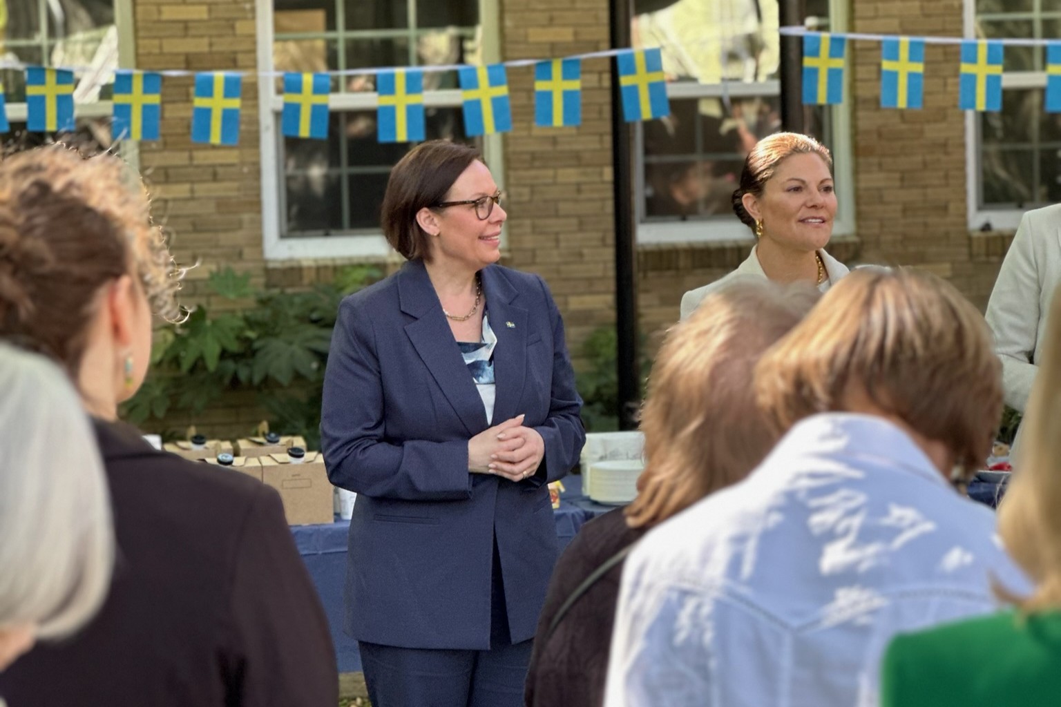 Utrikesministern och kronprinsessan står utomhus framför en girlang med svenska flaggor.