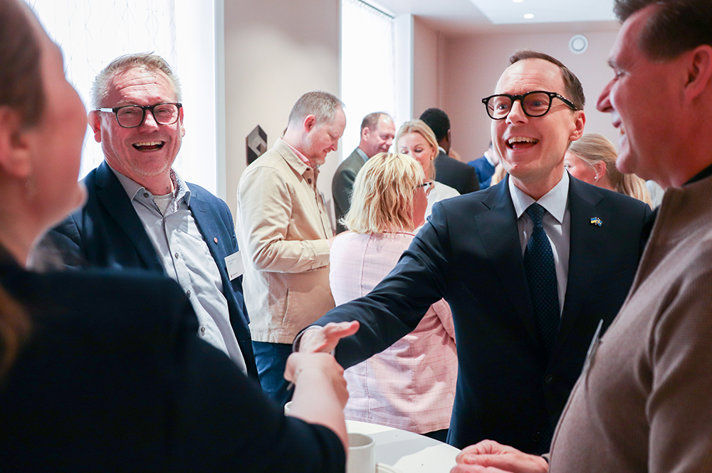 Två personer skakar hand med varandra. Ytterligare två personer står bredvid. Alla personer ser glada ut.