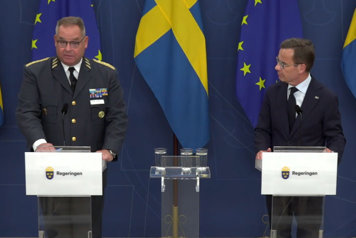 Statsminister Ulf Kristersson och Försvarsmaktens nästa överbefälhavare Michael Claesson i halvfigur vid var sin talpulpet och svenska flaggor i fonden.