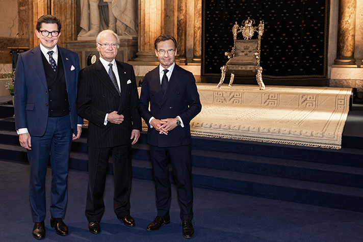 Talman Andreas Norlén, H.M. Konungen och statsminister Ulf Kristersson vid mottagningen på Kungliga slottet, ståendes framför en gåva från riksdag och regering – en matta komponerad av textilkonstnären Märta Måås-Fjetterström.