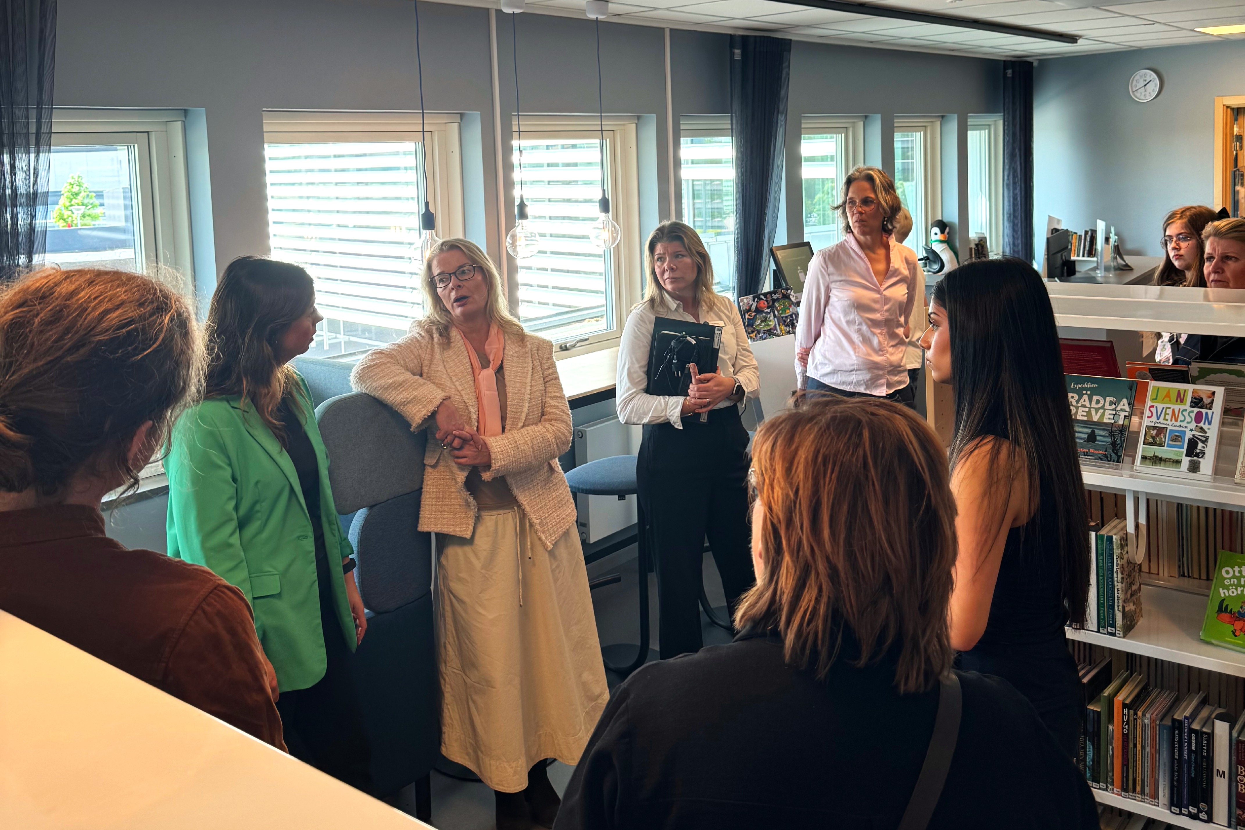 Skolministern och skolpersonalen står i ett skolbibliotek.
