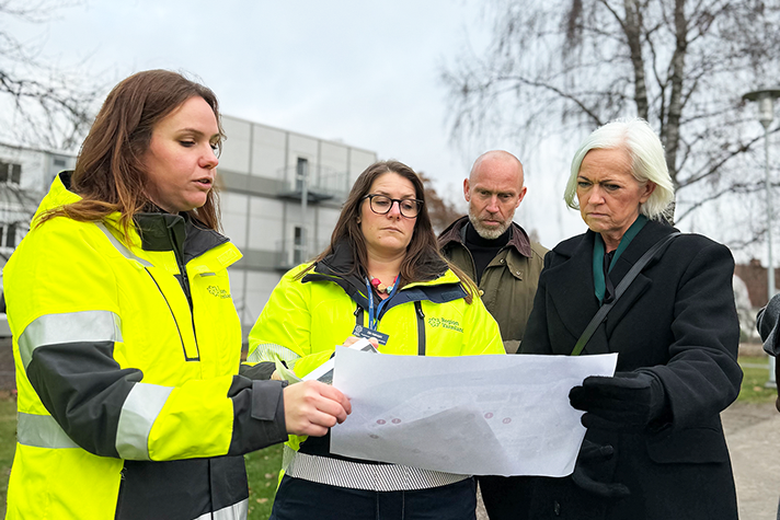 Fyra personer tittar på en ritning. Två av personerna bär arbetsjackor.