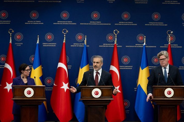 En kvinna och två män talar vid en presskonferens framför svenska och turkiska flaggor
