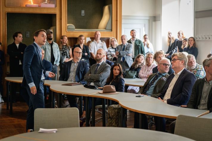 Mötesdeltagarna sitter i ett klassrum och samtalar.