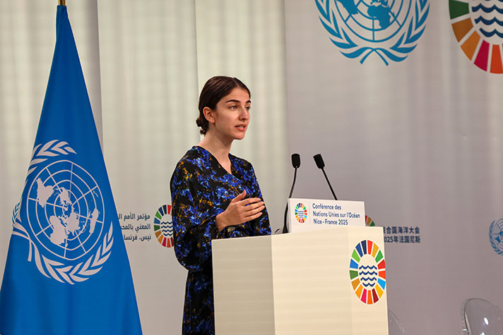 Ministern står i talarstolen intill FN-flaggan.