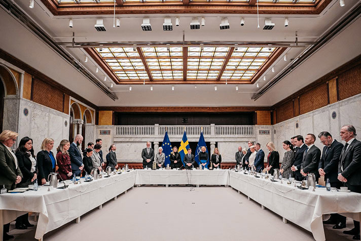 Regeringen och de inbjudna partiledarna för riksdagens partier iakttar en tyst minut stående längs med ett u-format bord i samband med torsdagens regeringssammanträde.