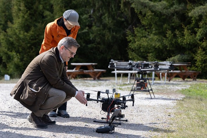 Två personer tittar på en drönare som står på marken.