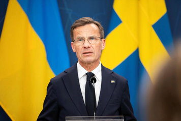 Statsministern i halvfigur framför Ukrainas och Sveriges flaggor.