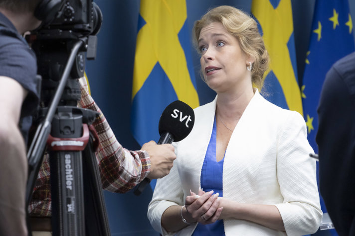Klimat- och miljöminister Annika Strandhäll intervjuas av  SVT. I bilden står ministern framför  två svenska flaggor och en EU-flagga. En kamera och en mikrofon som riktas mot ministern syns även i bildens vänstra halva.