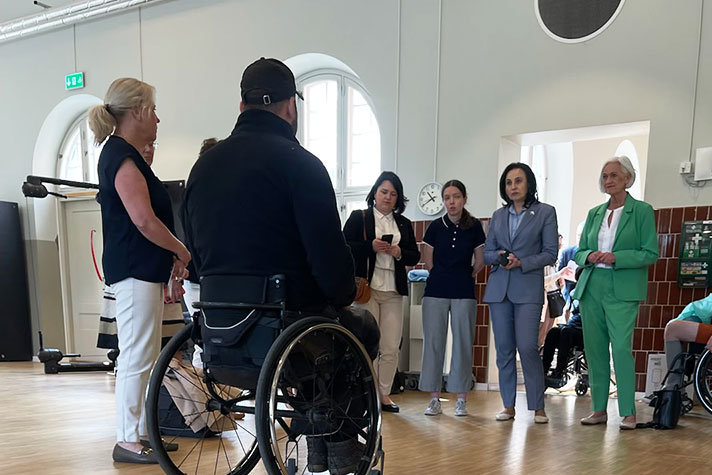I förgrunden en man i rullstol. Han pratar med ministrarna som står i bakgrunden.