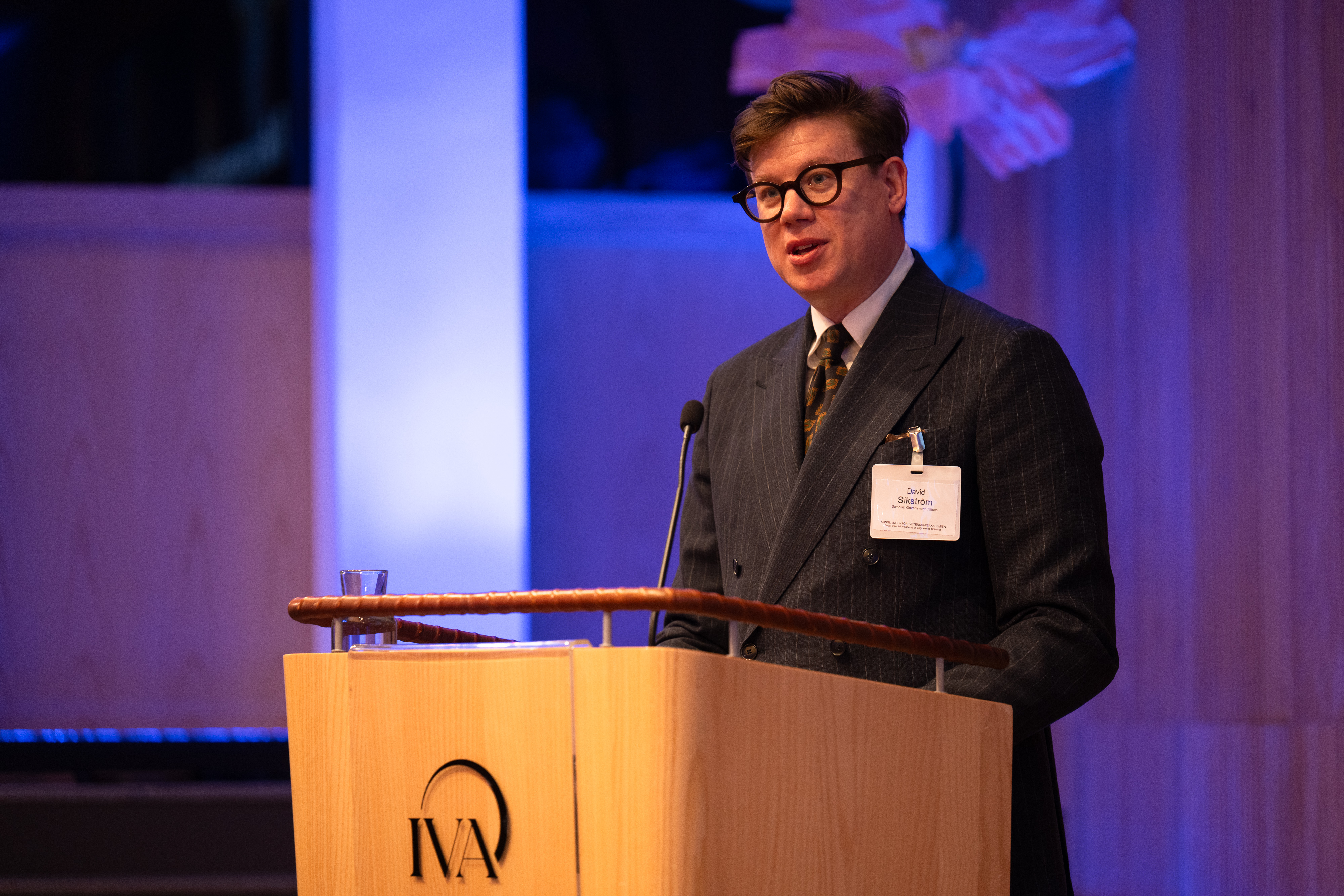 En man i kostym och glasögon talar vid en talarstol.