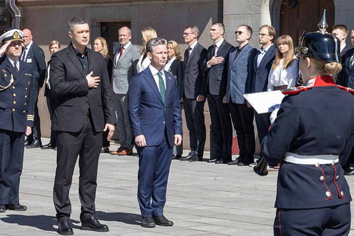 Mykhail Fedorov och Pål Jonson står sida vid sida. Fedorov har högra hand mot vänstra bröstet. De lyssnar på ukrainas nationalsång. I förgrunden ses en uniformerad musikant. I bakgrunden till vänster om statsråden syns en rad av människor som alla tittar rakt fram