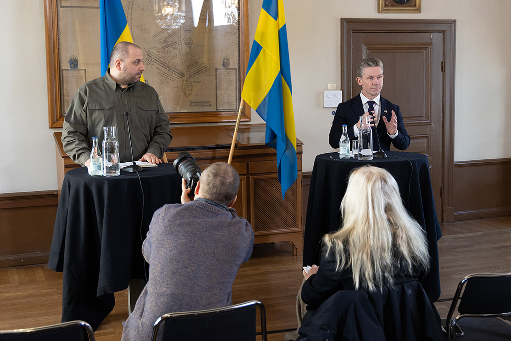 Pål Jonson pratar under pressträffen medans ukrainska försvarsministern Umjerov tittar på. Bakom ministrarna står den svenska och den ukrainska flaggan. 