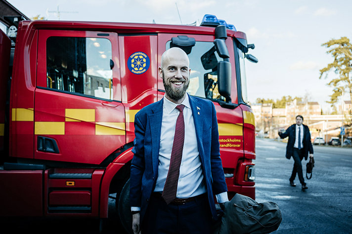 Carl-Oskar Bohlin är glad och står framför ena sidan av en brandbil. I bakgrunden syns statssekreterare Johan Berggren