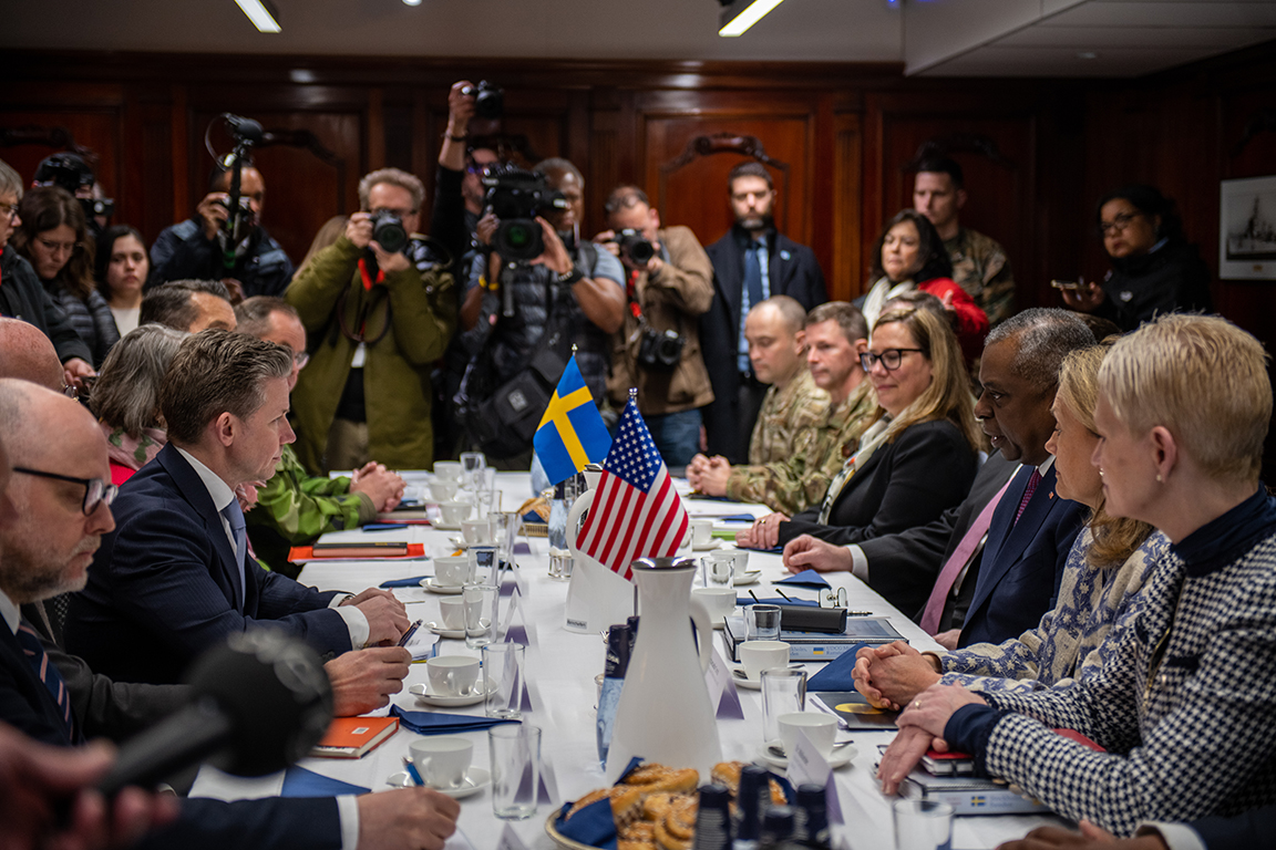 Försvarsminister Pål Jonson och försvarsminister Lloyd Austin håller ett möte dit många fotografer var inbjudna att delta de första fem minuterna. På varsin sida av bordet sitter svenska och amerikanska representanter. 