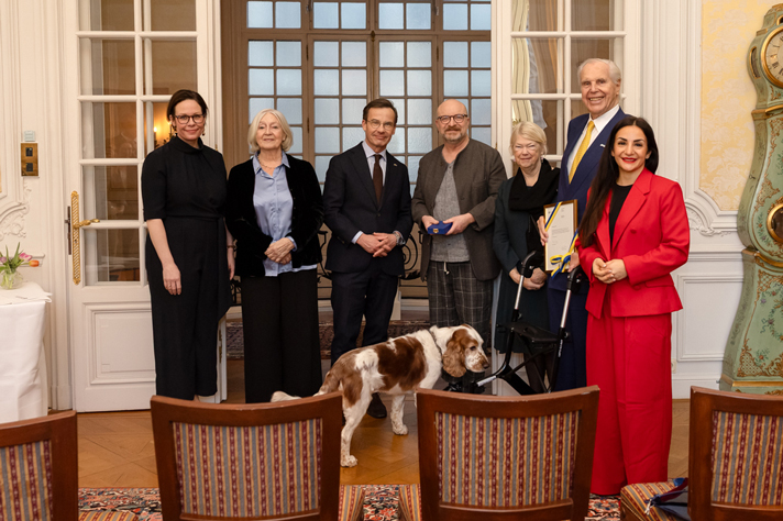 Gruppfoto av statsrådet Maria Malmer Stenergard, tidigare generaldirektören Inga-Britt Ahlenius, statsminister Ulf Kristersson, författaren och dramatikern Jonas Gardell, Lena Jersenius, projektledare för Hågkomstprojektet, SKMA m.m., entreprenören och mecenaten Anders Wall och statsrådet Parisa Liljestrand. 