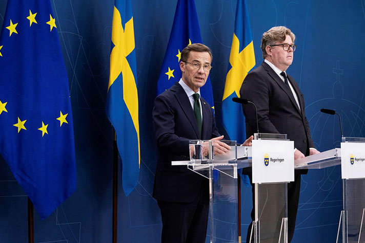 Statsminister Ulf Kristersson och justitieminister Gunnar Strömmer vid var sin talarstol  och svenska flaggor i fonden