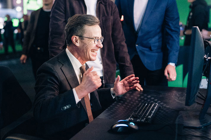 Statsminster Ulf Kristersson glad framför en datorskärm.