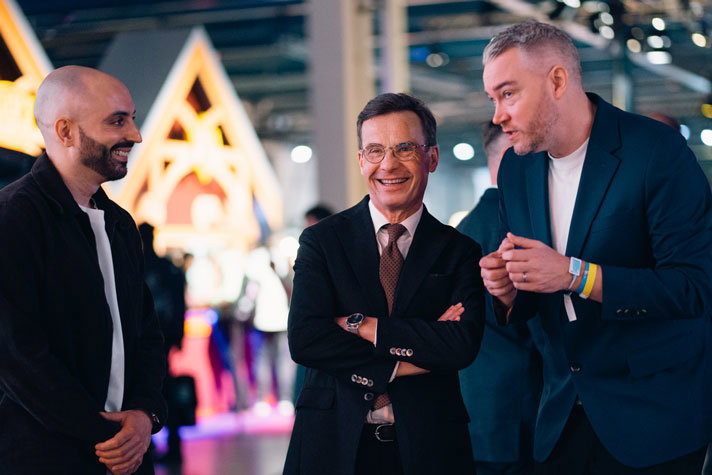 Ulf Kristersson står och pratar med två andra i Dreamhacks lokal med neonljus i bakgrunden.