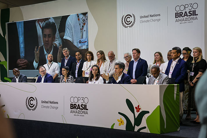 Ett antal människor står bakom ett stort konferensbord med logotyper på framsidan.