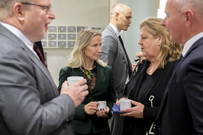 Flera personer står inomhus och pratar med varandra och dricker kaffe. 