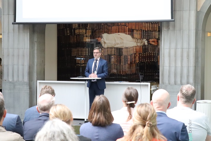 En man i kostym står och pratar framför en publik.