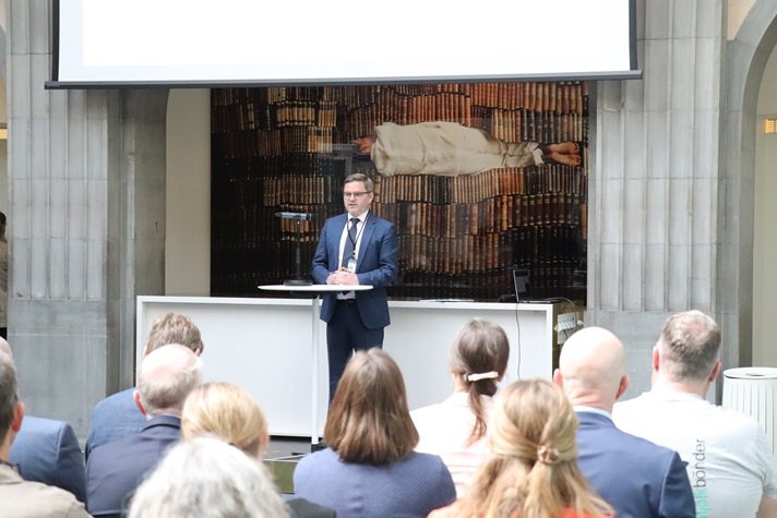 En man i kostym står och pratar framför en publik.