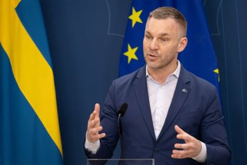 Erik Slottner står framför en svensk flagga och en EU-flagga och talar