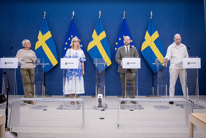 Fyra personer står på podiet vid en pressträff. I bakgrunden EU-flaggor och svenska flaggor.