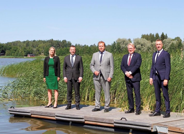 Sveriges, Finlands, Norges och Danmarks försvarsministrar samt Islands utrikesminister stående på en brygga i solljus.