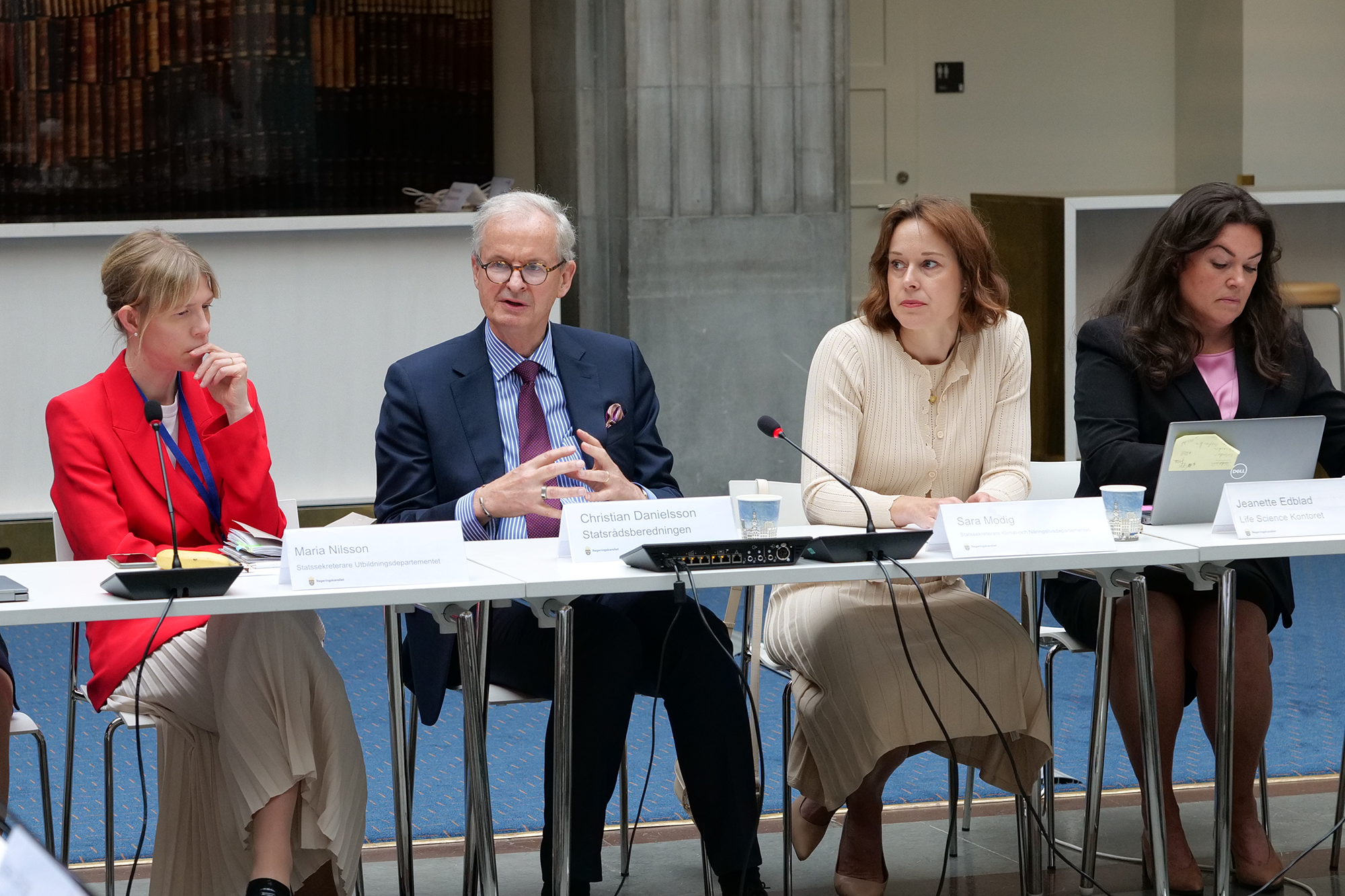 Fyra personer sitter bakom ett bord. En man mitten talar och gestikulerar med händerna.